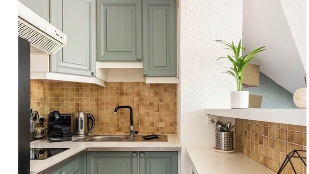 Una cucina con mobili color acquamarina, una parete rivestita di piastrelle, un lavello e una macchina per il caffè.