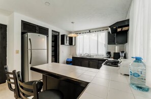 A modern kitchen with a refrigerator, stove, and sink. There is a dining table with chairs and a water dispenser. - Casa de lujo en Cancún con alberca privada y 4 recámaras (Cancún)