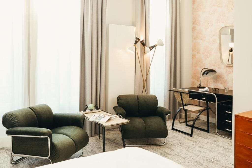 Ein Hotelzimmer mit einem Bett, zwei Sesseln, einem Schreibtisch und einer Lampe.