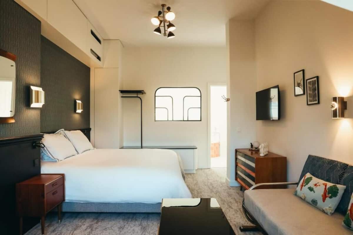 Ein modernes Hotelzimmer mit einem großen Bett, einer Couch, einem Schminktisch und einem Spiegel.