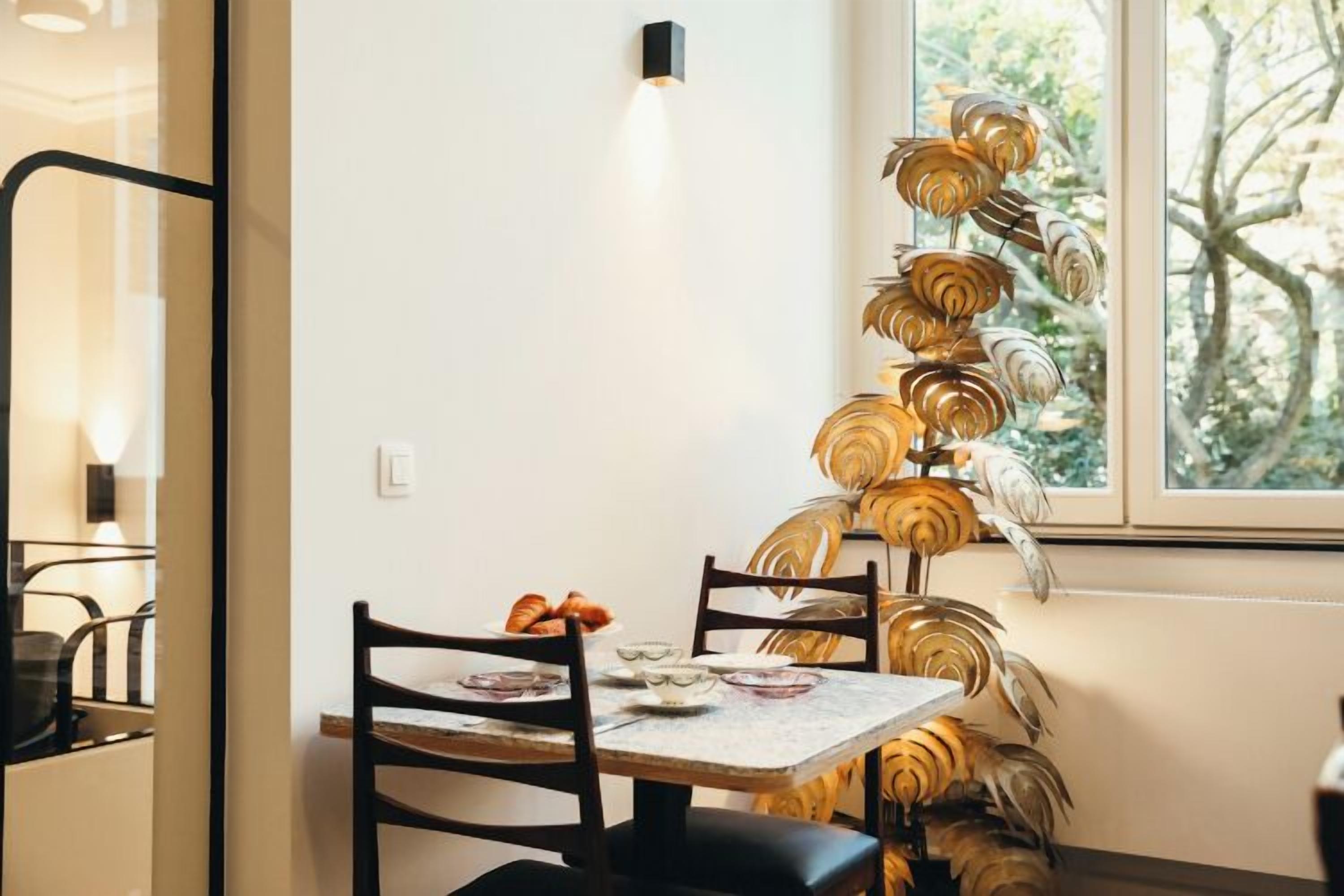 A dining area with a table set for two, a decorative wall piece, and a window with a view of trees.