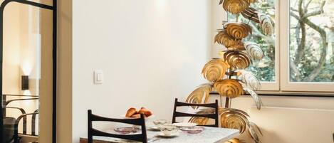 A dining area with a table set for two, a decorative wall piece, and a window with a view of trees.