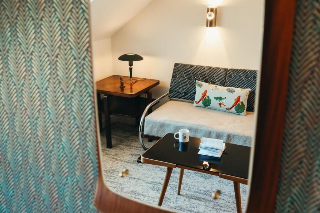 Hotelkamer met een bed, nachtkastje met een lamp, een klein tafeltje met een mok, en een kamerkleed met patroon.