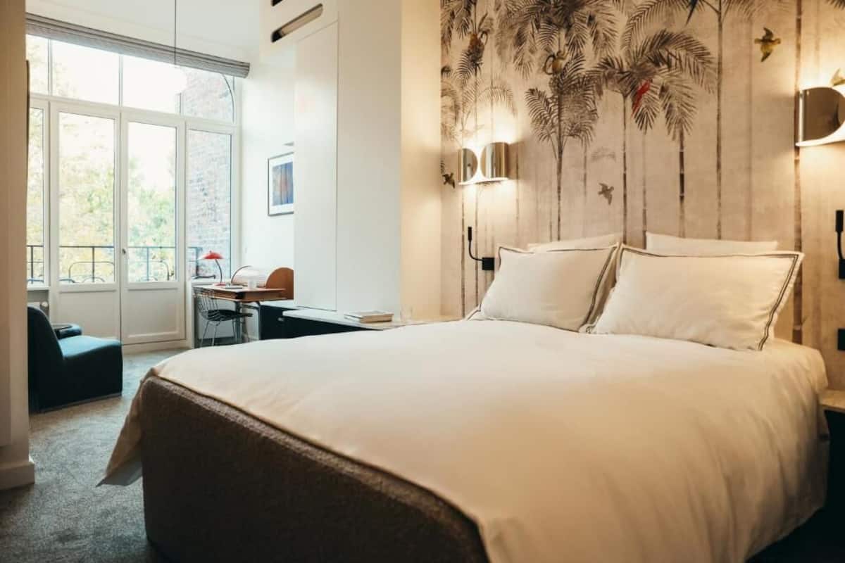 Ein Schlafzimmer mit einem großen Bett, einem Schreibtisch und einem Stuhl. Ein Fenster bietet Blick auf Bäume.