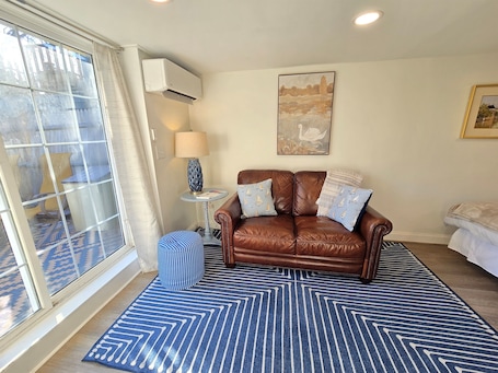 A cozy living room with a brown leather sofa, a patterned rug, and a large window with curtains.