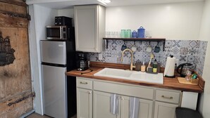 Cocina compacta con refrigerador, microondas y cafetera. Tiene una encimera de madera, un lavamanos y armarios con toallas colgadas.