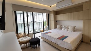 Een moderne slaapkamer met een groot bed, een klein krukje, een rieten stoel en uitzicht buiten door grote ramen.