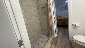 A bathroom with a shower, toilet, and a bed in the adjacent room. - #216 Polynesian - WALK 2 PIER PARK you and beach (Upper Grand Lagoon)