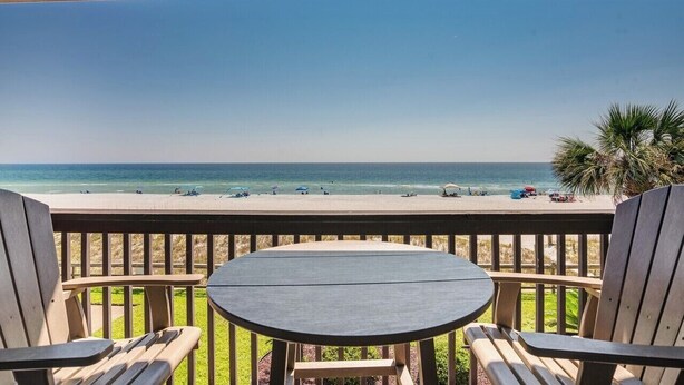 A wooden deck with a table and chairs overlooking a beach with people and umbrellas. - #216 Polynesian - WALK 2 PIER PARK you and beach (Upper Grand Lagoon)