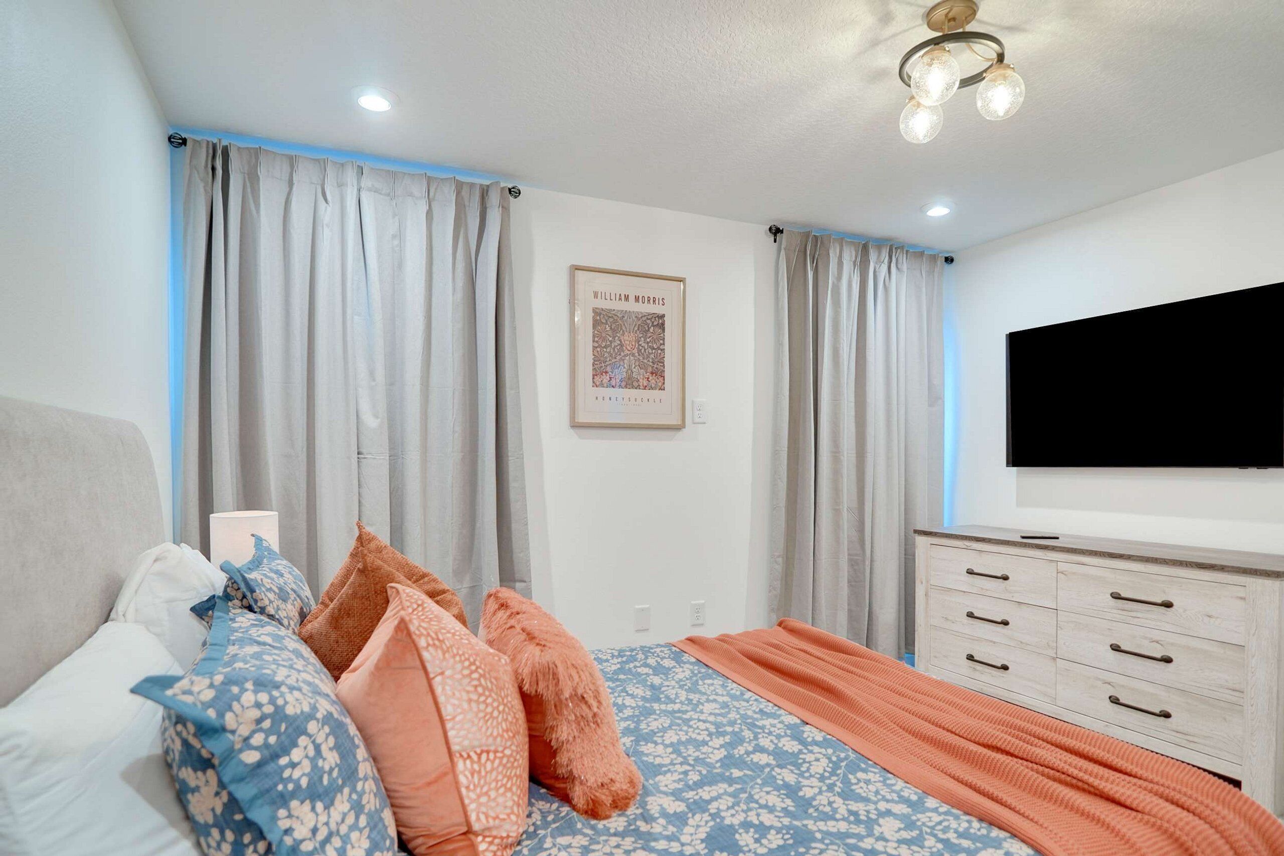 A bedroom with a bed, curtains, a framed picture, a dresser, and a TV.