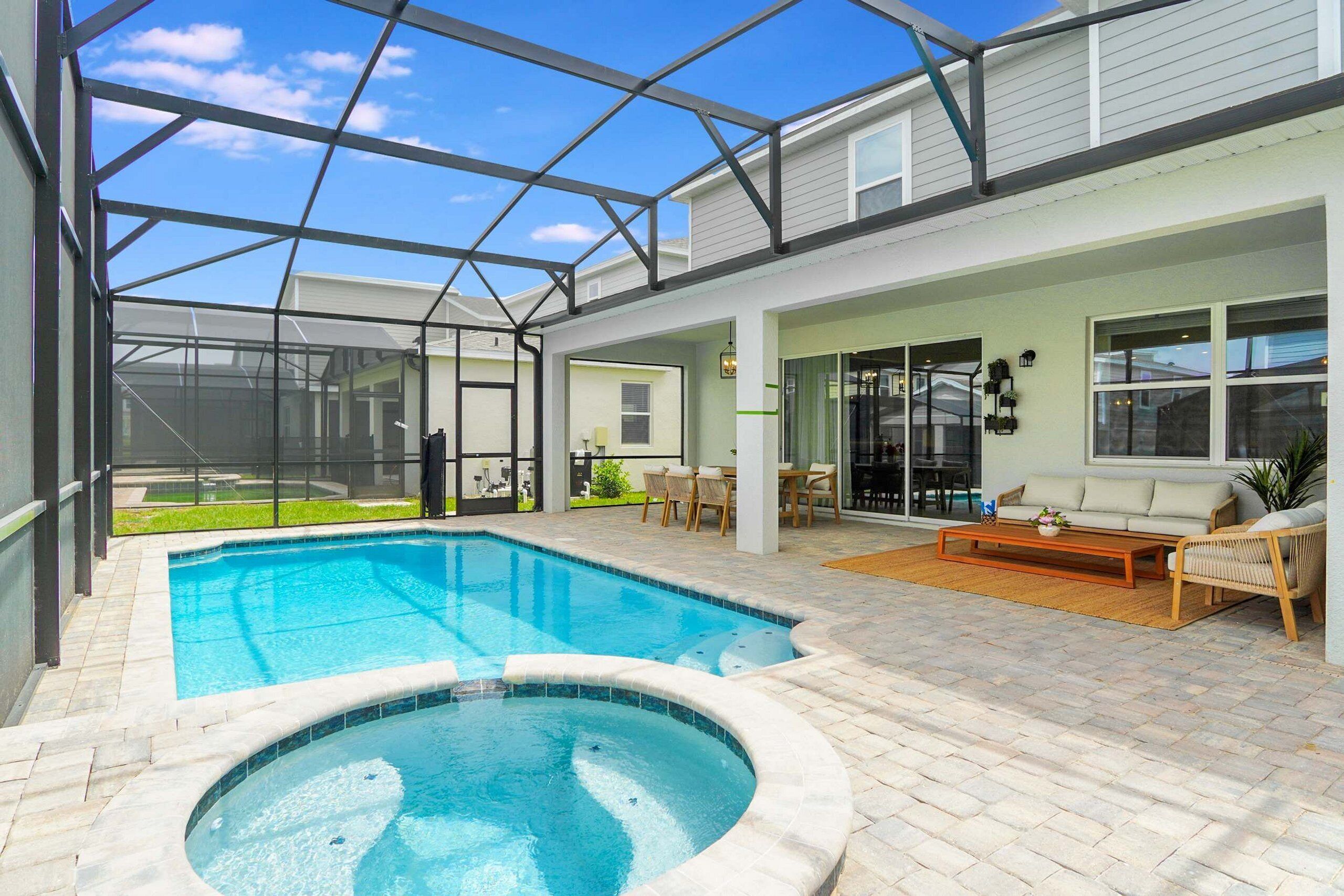 Une piscine extérieure couverte avec un jacuzzi, entourée d’un patio aménagé avec des sièges et offrant une vue sur un immeuble d’habitation.