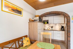 A kitchen with white cabinets, a brick archway, a microwave, and a dining area with a wooden table and bench. - Holiday Apartment "Henrich" with Terrace, Garden and Wi-Fi (Hooksiel)