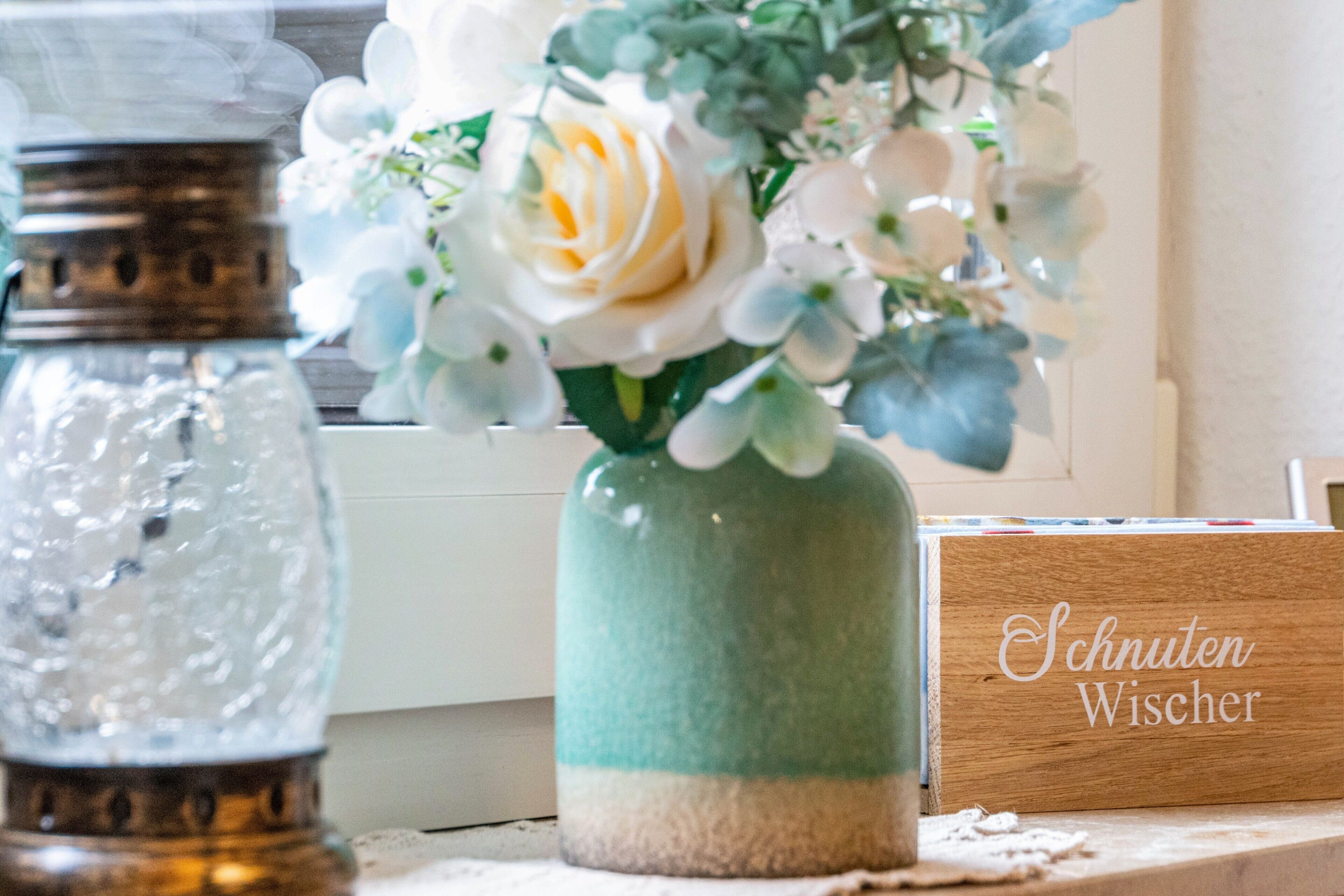 Eine dekorative Vase mit Blumen und ein Holzschild mit Text.