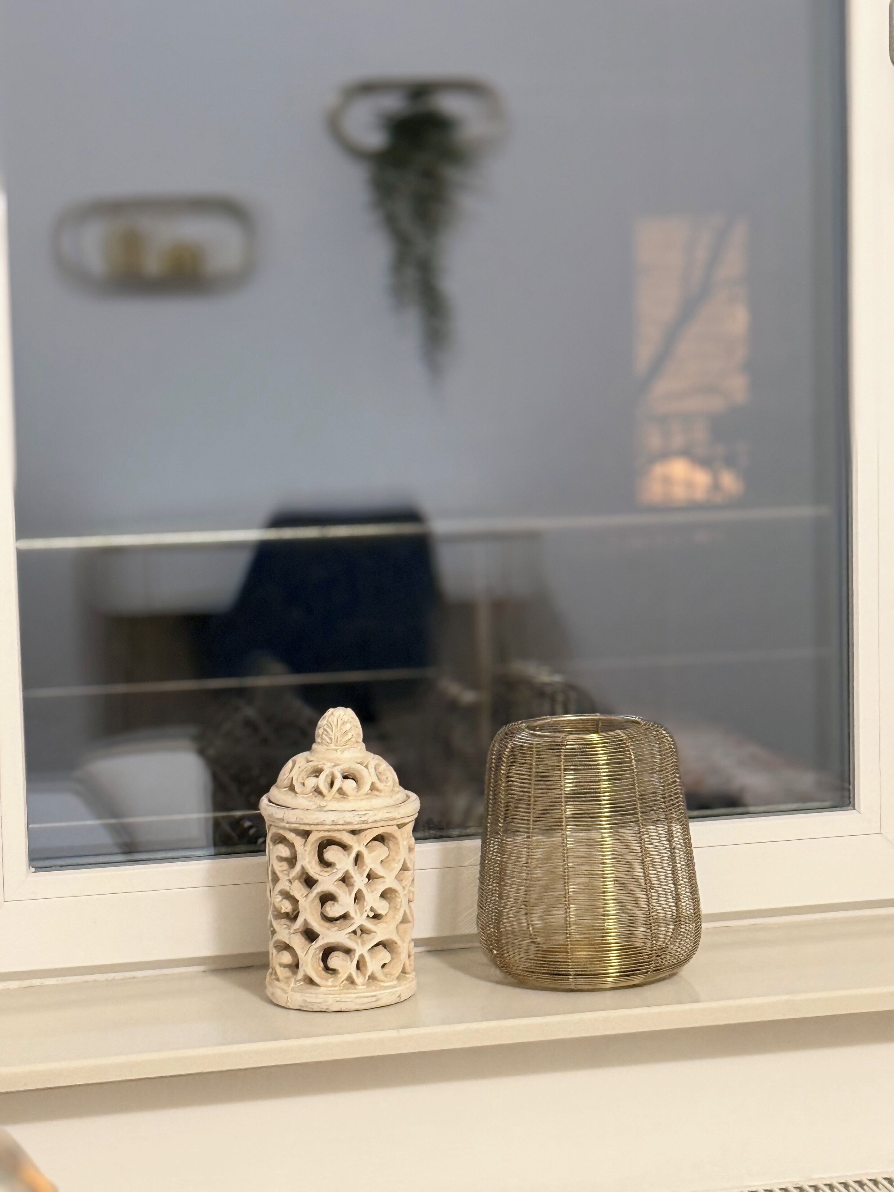 Ein Fensterbrett mit zwei dekorativen Behältern, einer mit aufwendigen Schnitzereien und der andere mit gewebtem Muster.