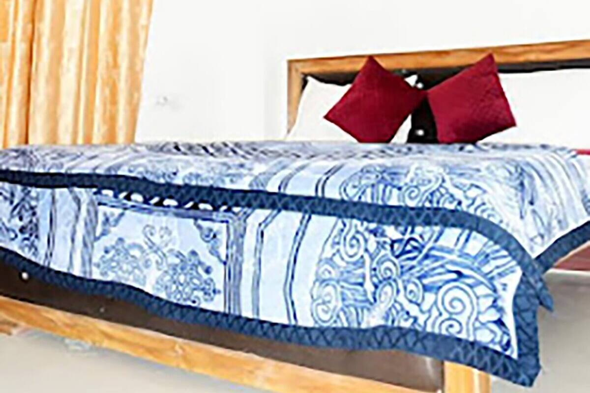 A bed with a patterned bedspread, wooden headboard, and two red pillows.