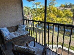 Ein Balkon mit einer Holzbänklä und einem Tisch, mit Blick auf ein Gewässer und Bäume.