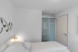 A bedroom with a bed, a wall-mounted light, a door, and a sliding glass door. - 5-Star Comfort Holiday Home Jümmers - 'Antje', Prime Location by the Wadden Sea National Park (Wangerland-Horumersiel)