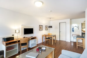 A modern living room with a flat-screen TV, a desk with a computer, a dining area with a table and chairs, and a sofa.