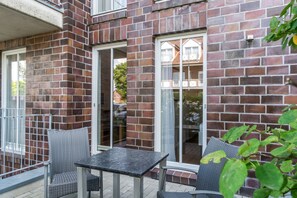 A brick exterior with a glass door and windows, outdoor seating with a table and chairs, and a small balcony.