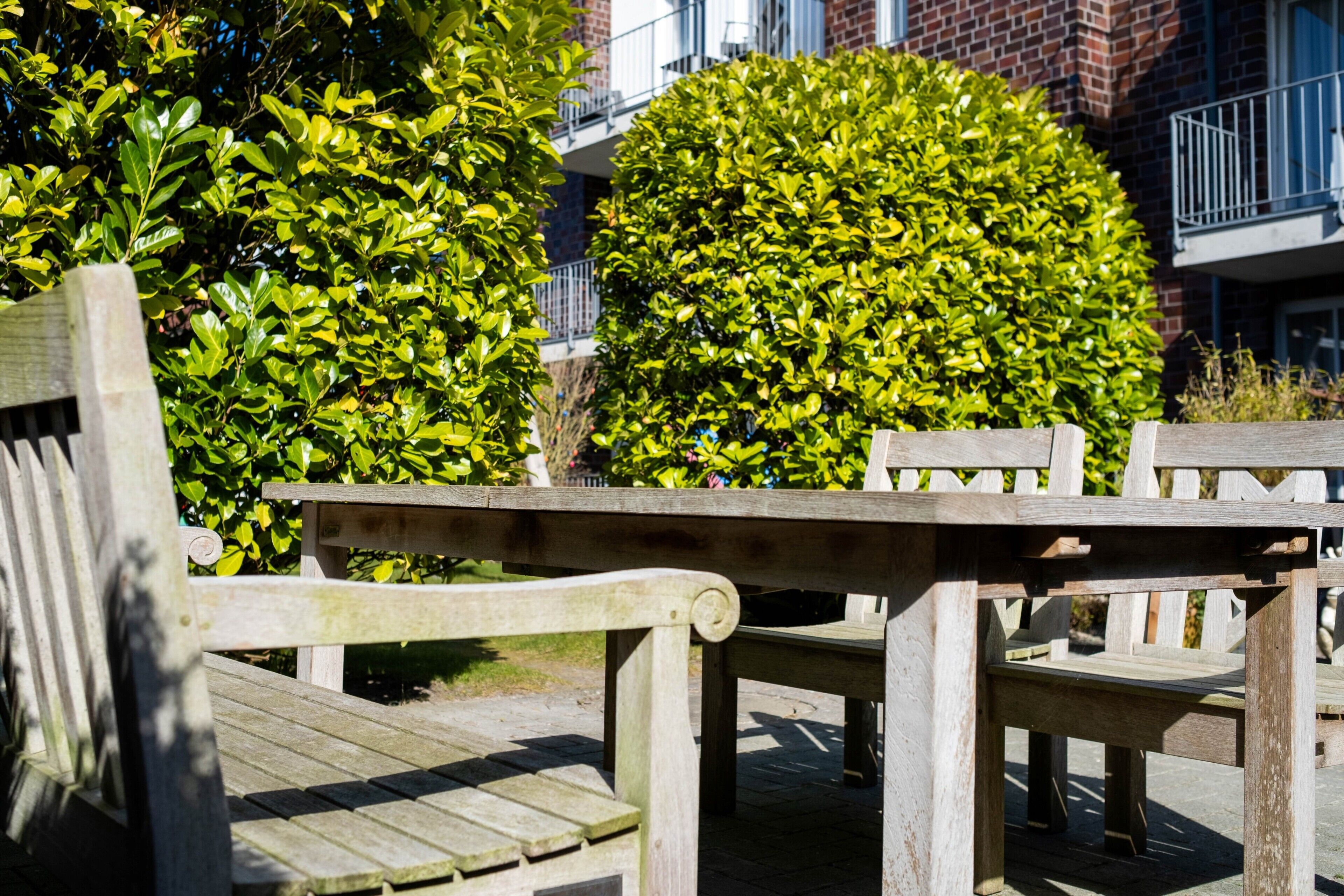 A wooden bench and table in an outdoor setting with a brick building and green foliage in the background.