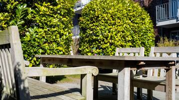 A wooden bench and table in an outdoor setting with a brick building and green foliage in the background.