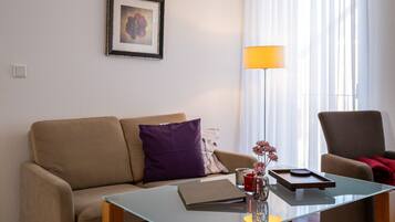 A living room with a sofa, a glass coffee table, a framed picture on the wall, a floor lamp, and a chair.