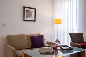 Ein Wohnzimmer mit einer Couch, einem Glastisch, einem gerahmten Bild an der Wand, einer Stehlampe und einem Sessel.