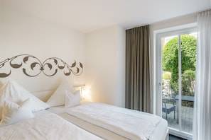 A hotel room with a bed, pillows, a wall decoration, a window with curtains, and a view of greenery outside.