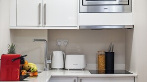 Una cocina moderna con armarios blancos, un microondas de acero inoxidable, un tostador rojo y un frutero.
