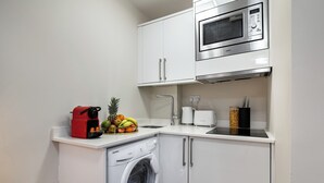 Cocina compacta con lavadora, microondas y frutero en la encimera.
