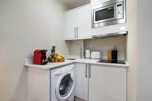 A compact kitchen with a washing machine, microwave, and a fruit bowl on the counter. - Cosy & Central Apt great for business and tourist (London)