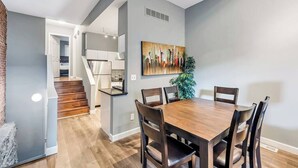 Una cocina moderna con una isla central, un área de comedor con una mesa y sillas de madera, y una escalera que sube a un nivel superior.