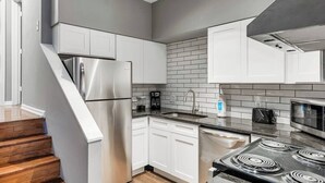 Una cocina moderna con armarios blancos, un refrigerador de acero inoxidable, una estufa a gas y un microondas.