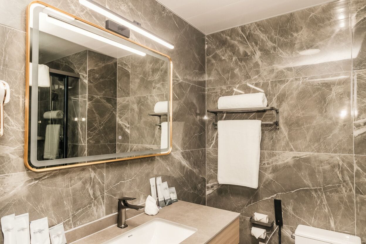 A modern bathroom with a marble wall, a large mirror, a sink, and a toilet.