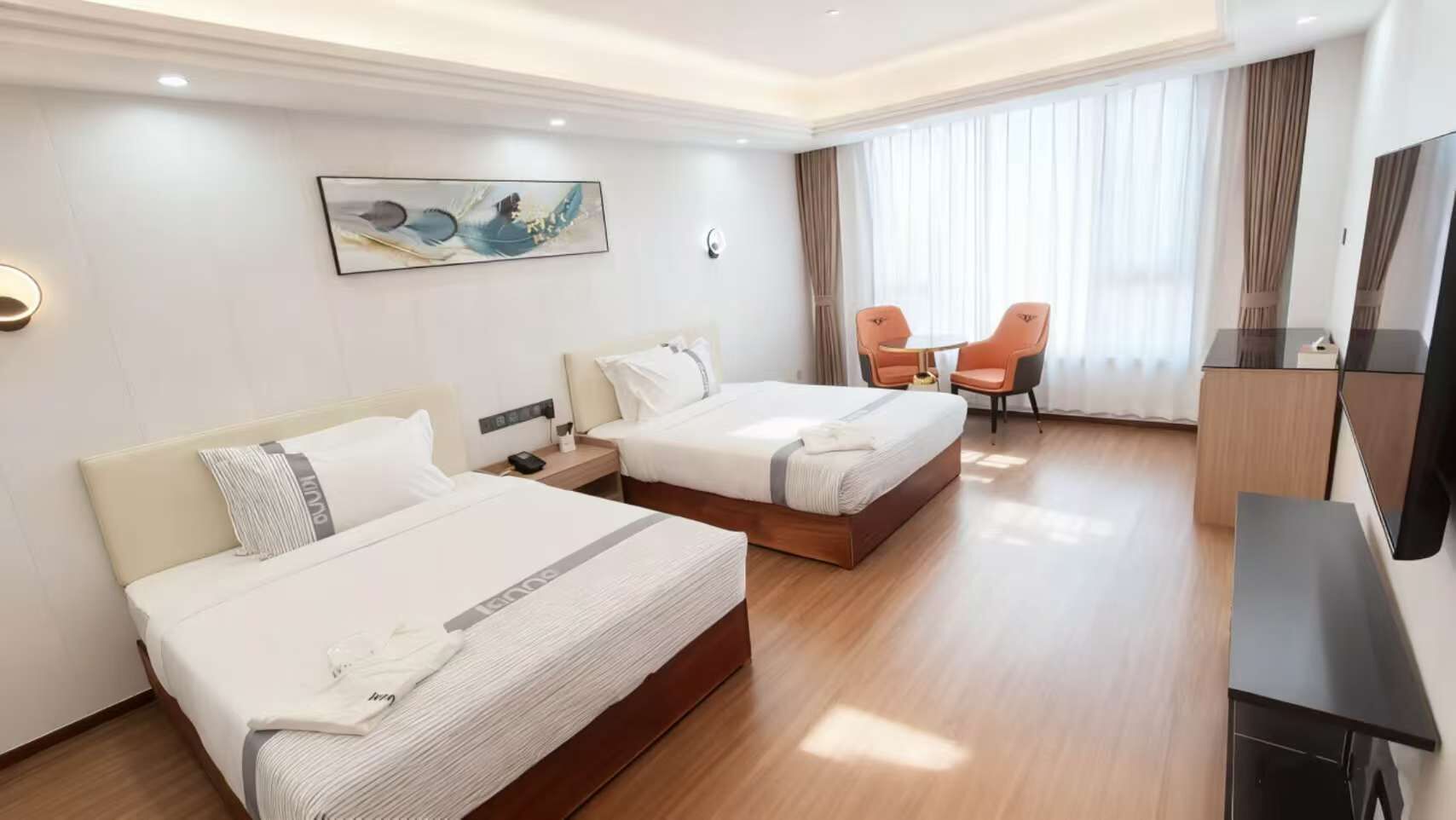 A hotel room with two beds, a desk, a chair, a TV, and a painting on the wall.
