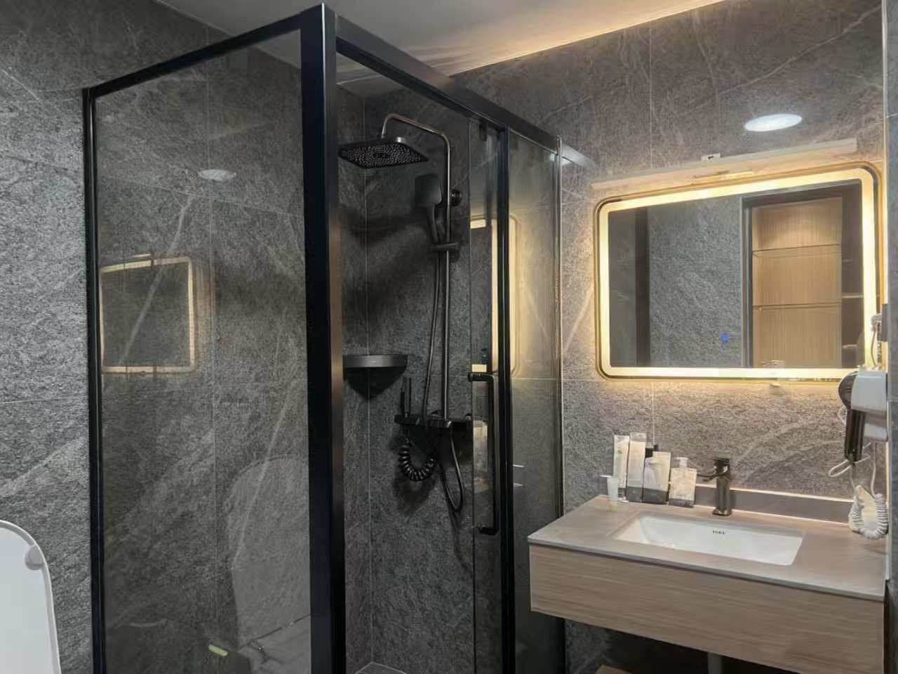 A modern bathroom with a glass-enclosed shower, a vanity with a mirror, and toiletries.