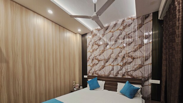 Una habitación de hotel moderna con una cama grande, paneles de madera en las paredes, un cabecero con diseño de mármol y un ventilador de techo.