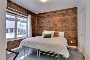 A bedroom with a bed, wooden walls, a window, and a view of buildings outside. - Condos Monts-Valin -153, rue du Massif (Valinouët) (Le Fjord-du-Saguenay Regional County Municipality)