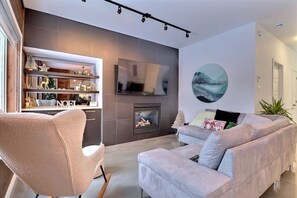 A modern living room with a fireplace, a television mounted on the wall, and a sofa with decorative pillows. - Condos Monts-Valin -153, rue du Massif (Valinouët) (Le Fjord-du-Saguenay Regional County Municipality)