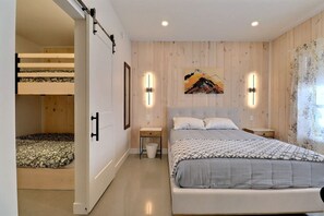 A bedroom with a bunk bed, a large bed, bedside tables, a wall-mounted light, and a painting. - Condos Monts-Valin - 47, rue du Sommet (Valinouët) (Saint-David-de-Falardeau)