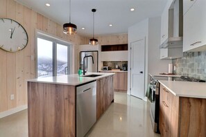 A modern kitchen with wooden cabinetry, stainless steel appliances, and pendant lighting. - Condos Monts-Valin - 47, rue du Sommet (Valinouët) (Saint-David-de-Falardeau)