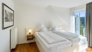 Un dormitorio con cama, mesita de noche, luz de pared y ventana con cortinas.