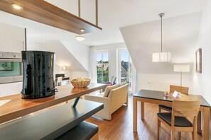 A modern kitchen with a coffee maker, a dining area with a table and chairs, and a sofa. - 5-Star Comfort Holiday Home Jümmers - 'Teetje', Prime Location by the Wadden Sea National Park (Wangerland-Horumersiel)