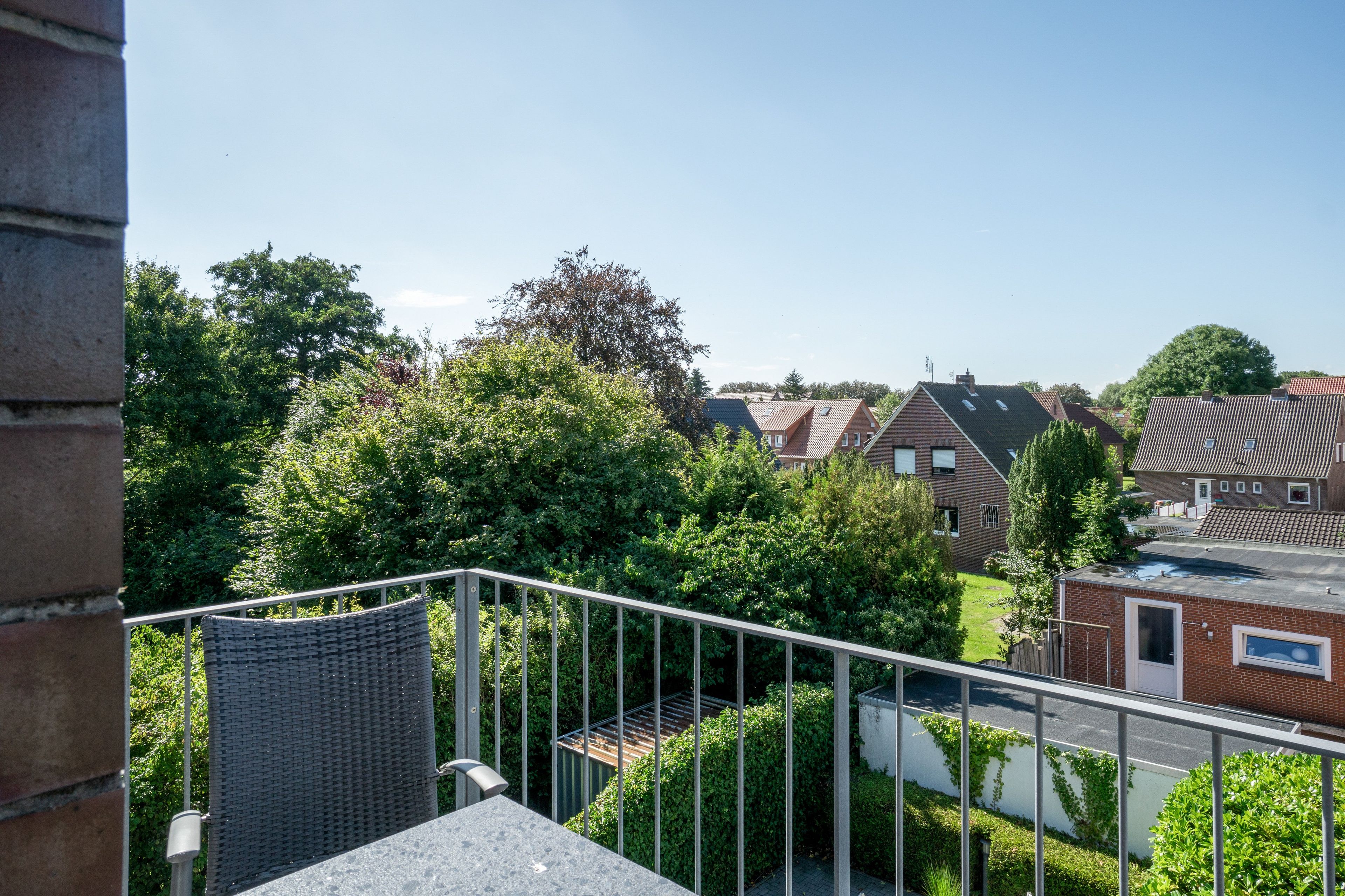 Ein Wohngebiet mit Häusern, einem Balkon mit Korbmöbeln und wolkenlosem Himmel.