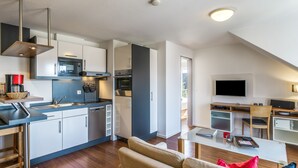 Una cocina moderna con electrodomésticos integrados, un comedor con mesa de vidrio y una sala de estar con sofá y televisor.