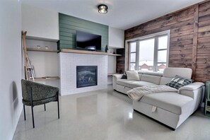A modern living room with a fireplace, a television, and a sofa. - Condos Monts-Valin - 27, rue du Sommet (Valinouët) (Saint-David-de-Falardeau)
