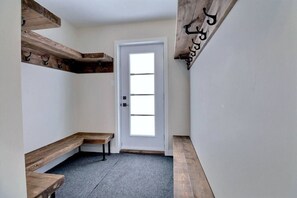 A hallway with a white door, wooden benches, and a wooden beam with a sign. - Condos Monts-Valin - 27, rue du Sommet (Valinouët) (Saint-David-de-Falardeau)