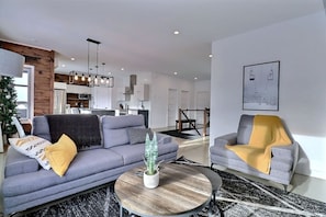 A modern living room with a grey sofa, a round coffee table, and a potted plant. - Condos Monts-Valin - 49, rue du Sommet (Valinouët) (Saint-David-de-Falardeau)