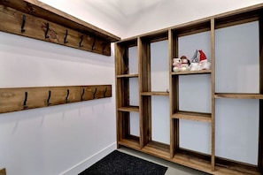 A hallway with wooden wall-mounted coat racks, a built-in shelving unit with decorative items, and a black doormat. - Condos Monts-Valin - 49, rue du Sommet (Valinouët) (Saint-David-de-Falardeau)