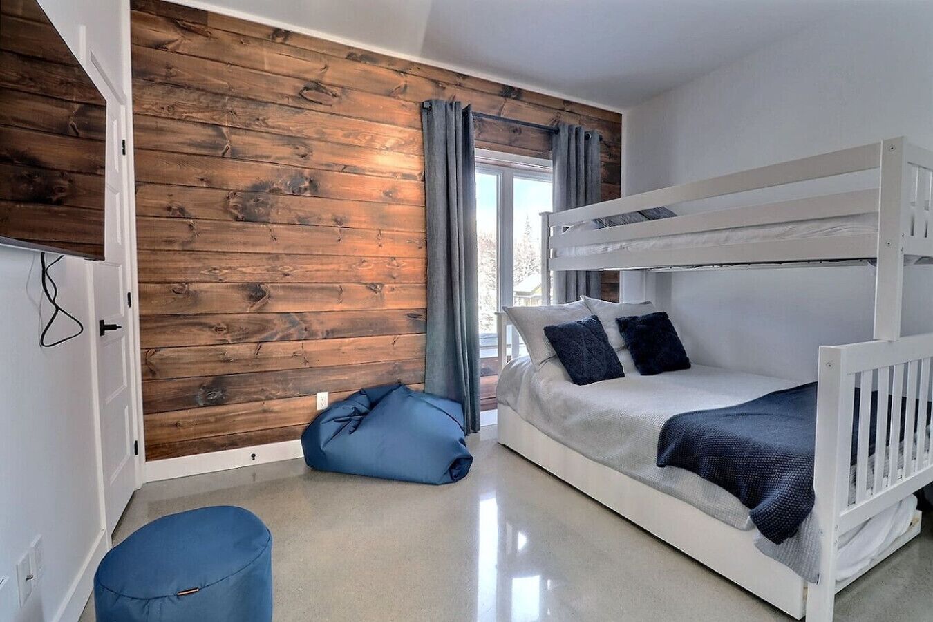 Une chambre avec un lit superposé, un fauteuil en forme de poire bleu et un mur en bois.